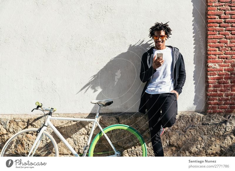 Afrojunger Mann mit Handy und festem Fahrrad. Jugendliche Afrikanisch schwarz Mulatte Afro-Look Mobile Fixie Telefon Lifestyle stehen Fahrradfahren benutzend