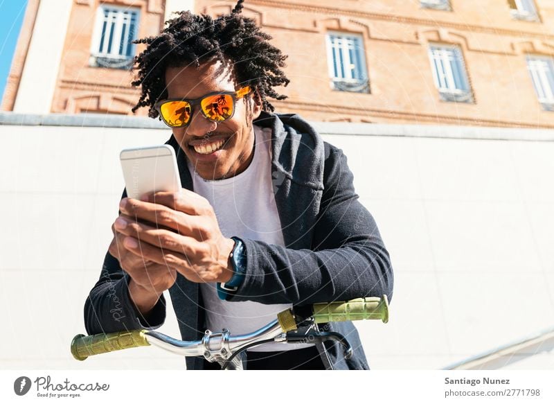 Afrojunger Mann mit Handy und festem Fahrrad. Jugendliche Afrikanisch schwarz Mulatte Afro-Look Mobile Fixie Telefon Lifestyle stehen Fahrradfahren benutzend