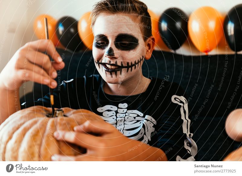 Ein fröhlicher Junge verkleidet, der zu Hause einen Kürbis schmückt. Halloween Kind malen Skelett Freude Familie & Verwandtschaft Hermano Porträt Angst