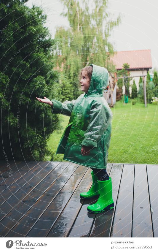 Kleines Mädchen, das im Regen steht und einen grünen Regenmantel trägt. Lifestyle Freude Glück Sommer Kind Mensch Frau Erwachsene Kindheit Wetter Mantel Stiefel