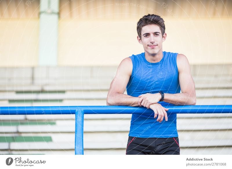 Junger Mann in Sportbekleidung, der sich auf einen Metallzaun lehnt und sich auf der Bühne posiert. Stadion sportlich Körperhaltung ruhen Sportler Fitness