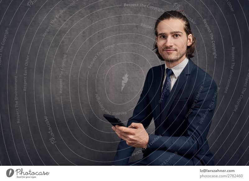 Hübscher junger Mann mit langen Haaren, der einen schicken Anzug und eine blaue Krawatte trägt rollen Stil Gesicht lesen Erfolg Business PDA