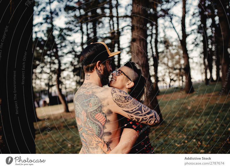 Junger Mann mit Tattoos umarmt die Dame im Wald. Paar Umarmen Schnappschuss Park ohne Hemd Typ Jugendliche Schickimicki umarmend Frau romantisch Kunst