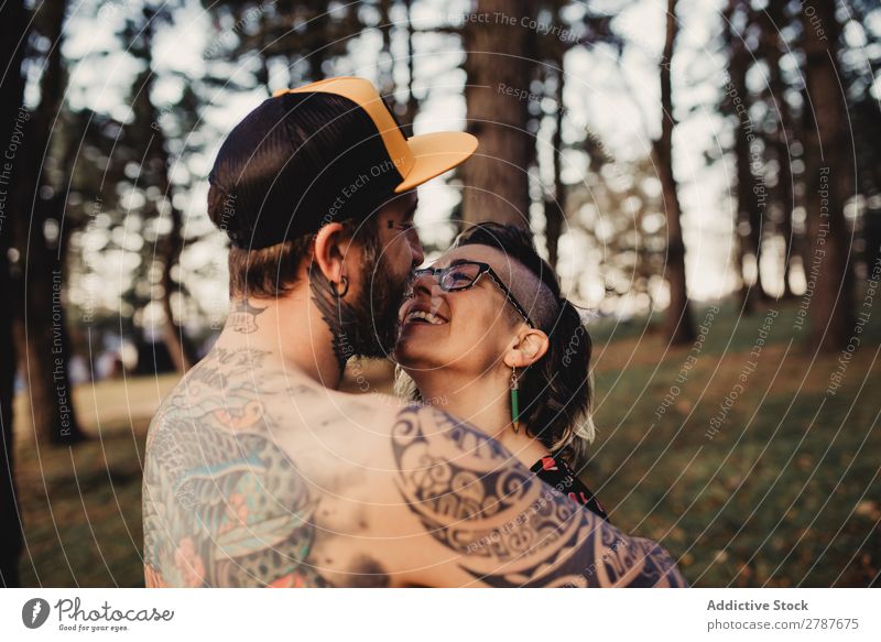 Junger Mann mit Tattoos umarmt die Dame im Wald. Paar Umarmen Schnappschuss Park ohne Hemd Typ Jugendliche Schickimicki umarmend Frau romantisch Kunst