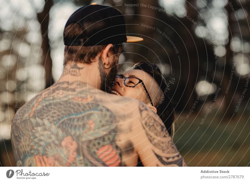 Junger Mann mit Tattoos umarmt die Dame im Wald. Paar Umarmen Schnappschuss Park ohne Hemd Typ Jugendliche Schickimicki umarmend Frau romantisch Kunst