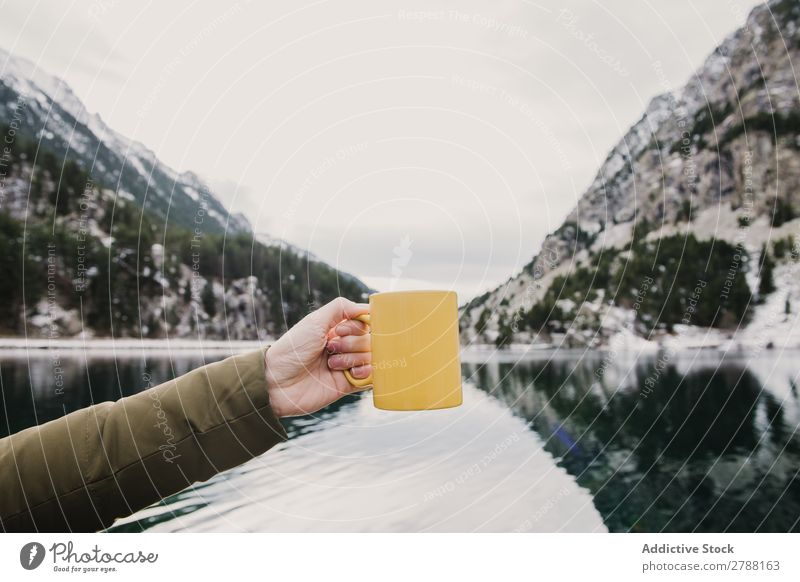 Person mit Becher in der Nähe eines wunderschönen Sees zwischen Hügeln im Schnee und bewölktem Himmel. Mensch Pyrenäen Wolken Tasse wunderbar Berge u. Gebirge