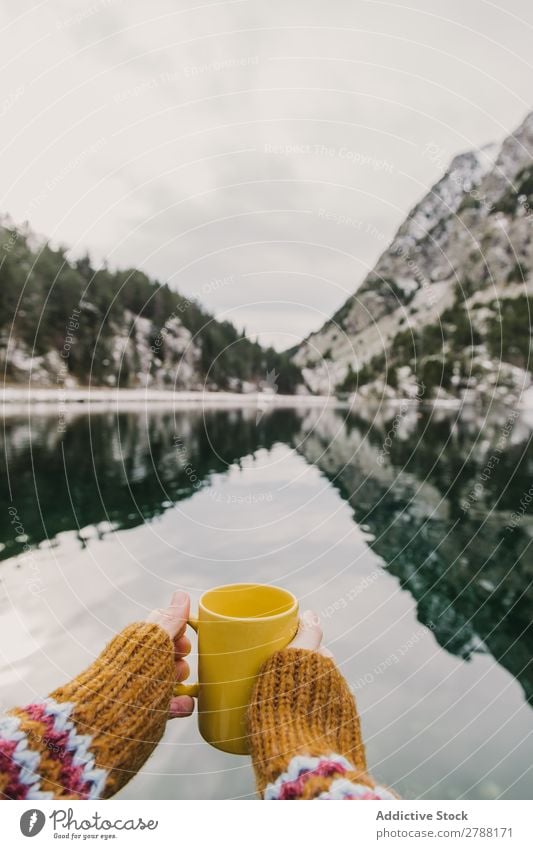 Person mit Becher in der Nähe eines wunderschönen Sees zwischen Hügeln im Schnee und bewölktem Himmel. Mensch Pyrenäen Wolken Tasse wunderbar Berge u. Gebirge