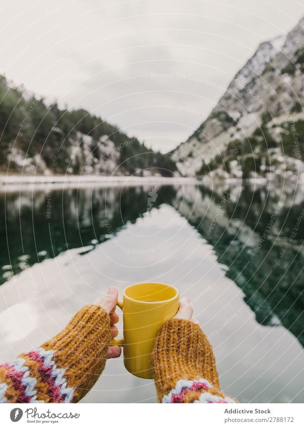 Person mit Becher in der Nähe eines wunderschönen Sees zwischen Hügeln im Schnee und bewölktem Himmel. Mensch Pyrenäen Wolken Tasse wunderbar Berge u. Gebirge