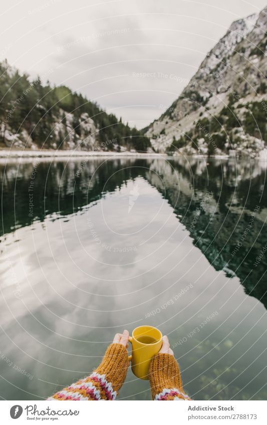 Person mit Becher in der Nähe eines wunderschönen Sees zwischen Hügeln im Schnee und bewölktem Himmel. Mensch Pyrenäen Wolken Tasse wunderbar Berge u. Gebirge