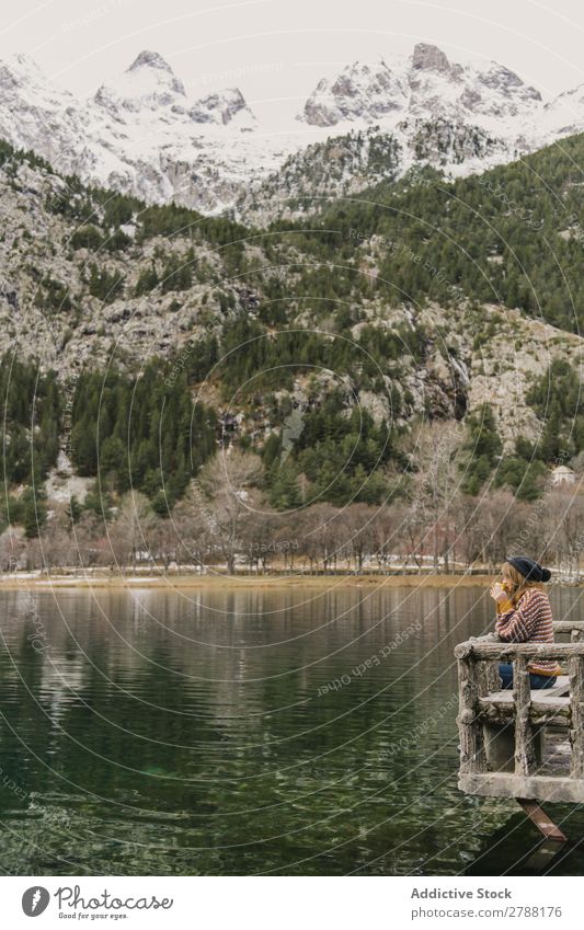 Frau auf Sitz in der Nähe des wunderschönen Sees zwischen Hügeln im Schnee und bewölktem Himmel. Pyrenäen wunderbar Wasser Oberfläche Berge u. Gebirge Wolken