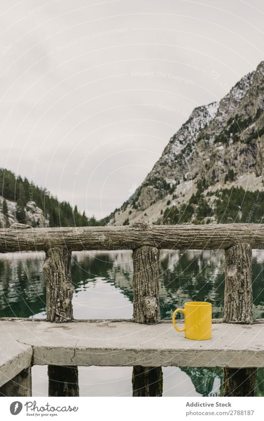 Cup auf dem Sitzplatz in der Nähe des wunderschönen Sees zwischen Hügeln im Schnee und bewölktem Himmel. Tasse Pyrenäen wunderbar Wasser Oberfläche