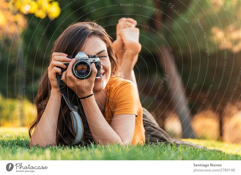 Lächelnde junge Frau, die eine Kamera benutzt, um im Park zu fotografieren. Fotograf Fotografie Fotokamera Jugendliche Mädchen digital weiß Freizeit & Hobby 1