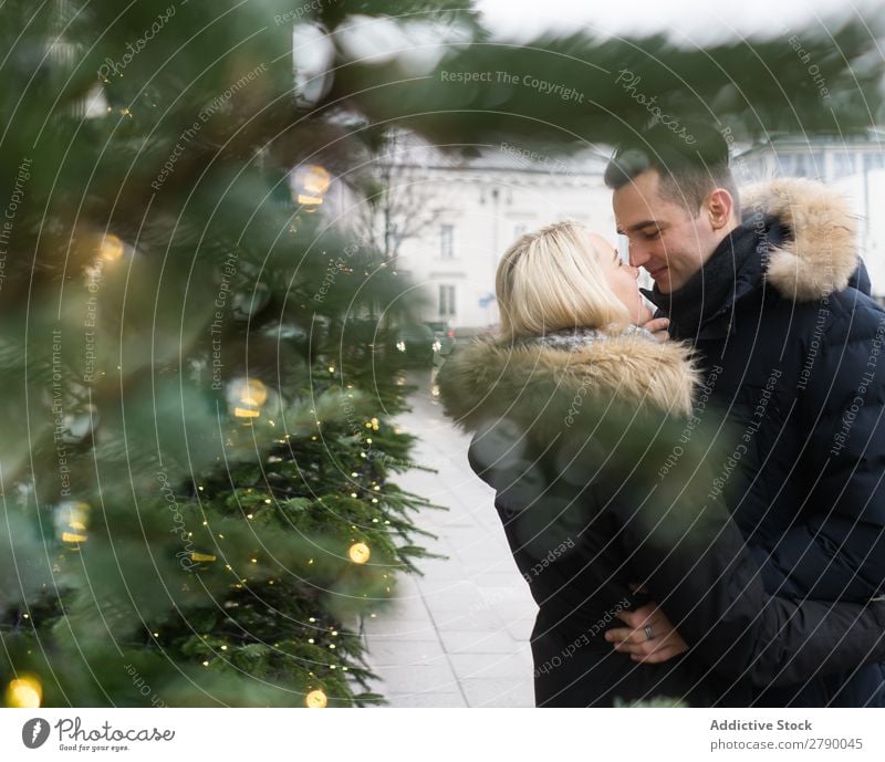 Lächelndes Paar, das Spaß auf der Straße in der Nähe einer Tanne mit Feenlicht hat. Spaß haben Lichterkette Weihnachten & Advent Baum Typ Dame Skijacke Glück