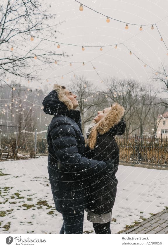 Lächelndes Paar, das Spaß auf der Straße in der Nähe eines Baumes mit Lichterketten hat. Spaß haben Weihnachten & Advent Typ Dame Skijacke Glück Hand Holz