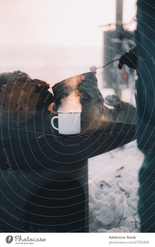 Getreideperson in der Nähe des Ofens mit Metallbecher Mensch Tasse Schmelzofen Winter Landschaft heizen Getränk heiß Arktis kalt Schnee Temperatur Wasserdampf