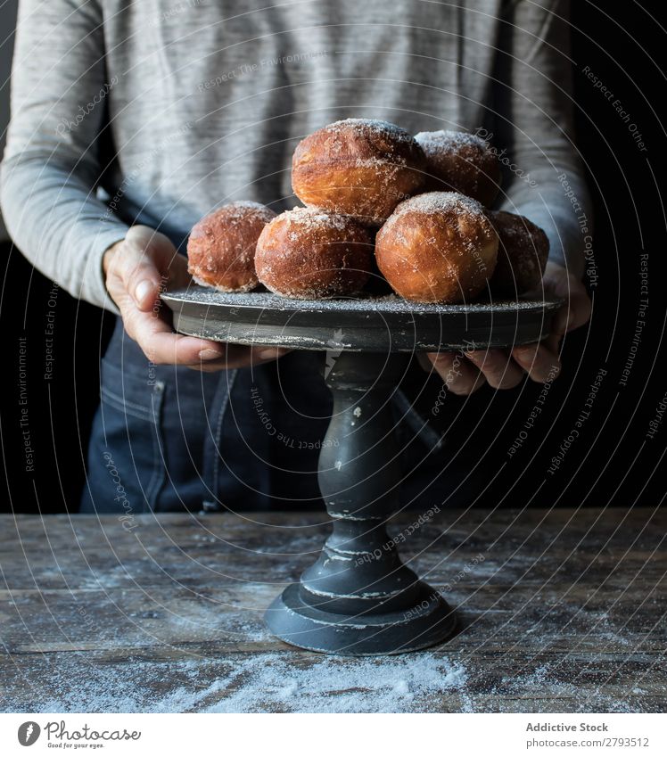 Person in der Nähe von gebackenen Kuchen auf dem Ständer auf dem Tisch Mensch Tablett Brotlaib Zucker gepulvert Dunkelheit Lebensmittel Holz Backwaren Kulisse