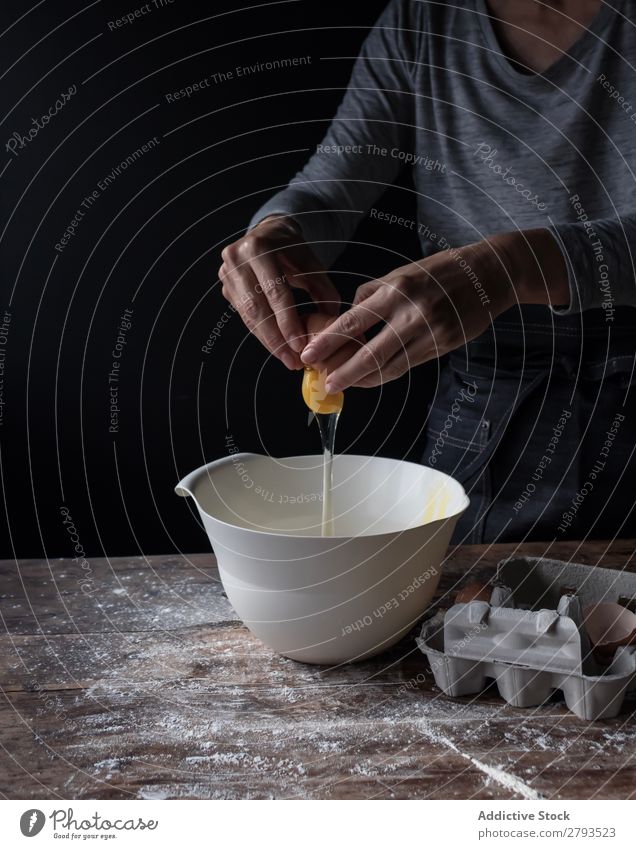 Person, die das Ei in der Schüssel auf dem Tisch knackt. Schalen & Schüsseln kochen & garen Mehl Rissbildung Holz Mahlzeit Handwerk brechen geschmackvoll Mensch