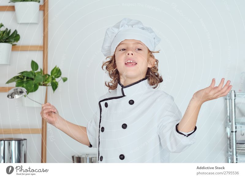 Junge mit Kochmütze, der die Schöpfkelle hält und den Daumen in der Küche zeigt. Schöpflöffel Daumen hoch Küchenchef Kind Hut Coolness gestikulieren