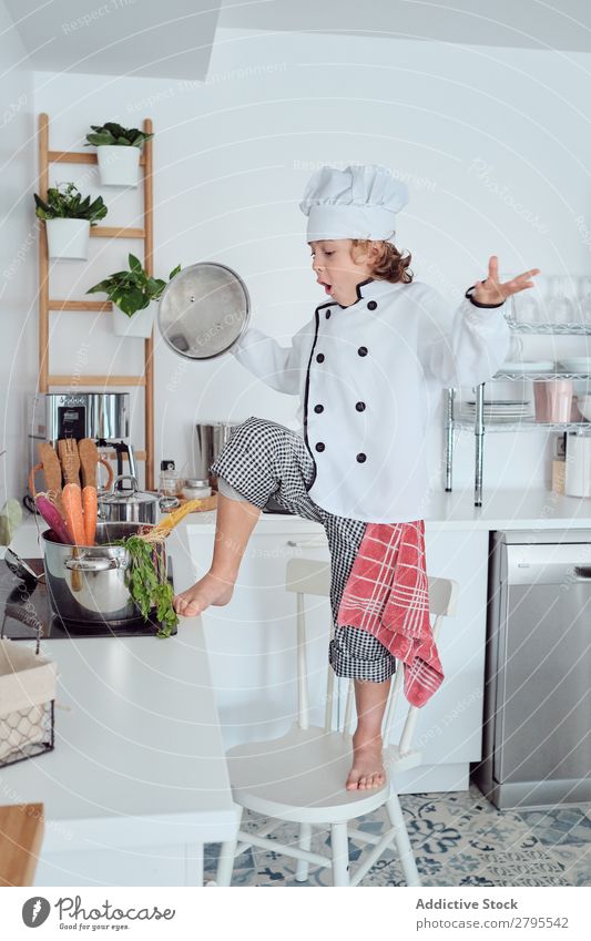 Junge mit Kochmütze mit Deckel neben dem Topf auf Stuhl in der Küche überdeckt Küchenchef Kind Gemüse Hut kochen & garen modern lustig heimwärts Licht