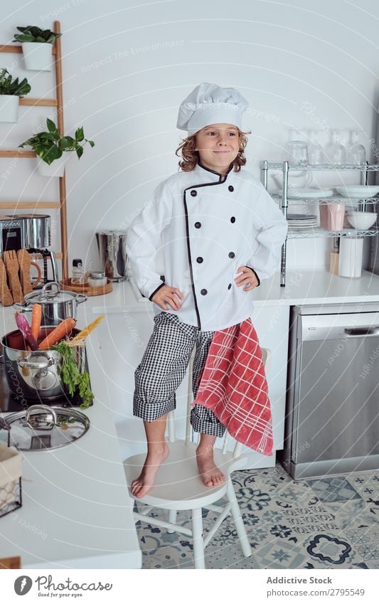 Junge mit Kochmütze in der Küche Möhre Küchenchef Kind Gemüse Hut frisch zeigen Hand Hüfte kochen & garen modern lustig heimwärts Licht vorbereitend