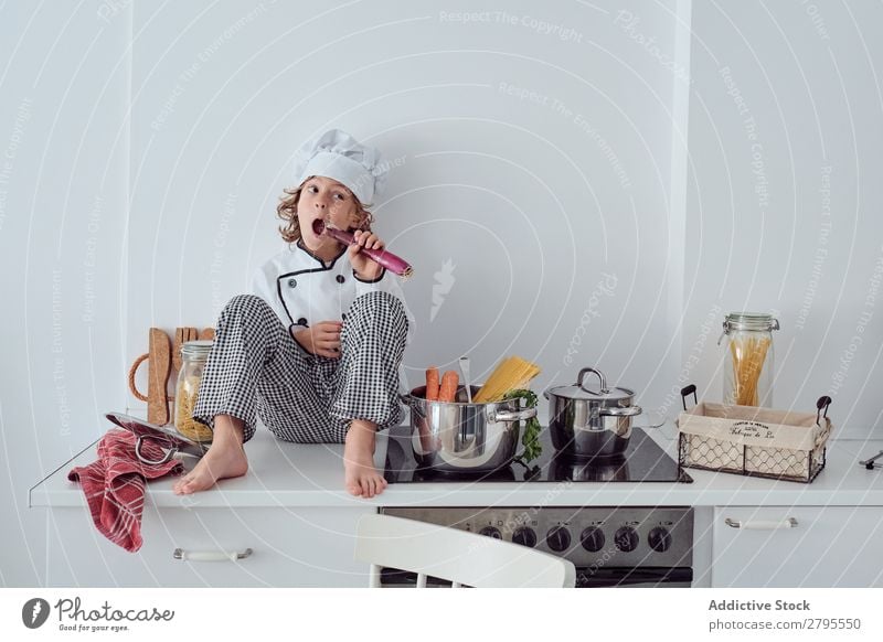 Junge mit Kochmütze neben Töpfen auf der Elektrofritteuse in der Küche sitzend Topf Küchenchef Kind Gemüse Hut Herd & Backofen kochen & garen modern lustig