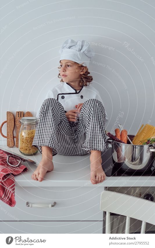 Junge mit Kochmütze neben Töpfen auf der Elektrofritteuse in der Küche sitzend Topf Küchenchef Kind Gemüse Hut Herd & Backofen kochen & garen modern lustig