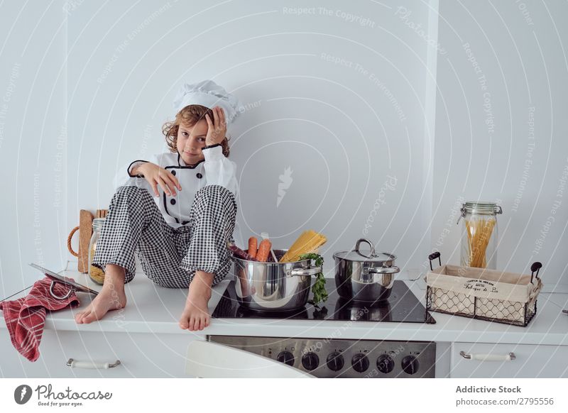 Junge mit Kochmütze neben Töpfen auf der Elektrofritteuse in der Küche sitzend Topf Küchenchef Kind Gemüse Hut Herd & Backofen kochen & garen modern lustig