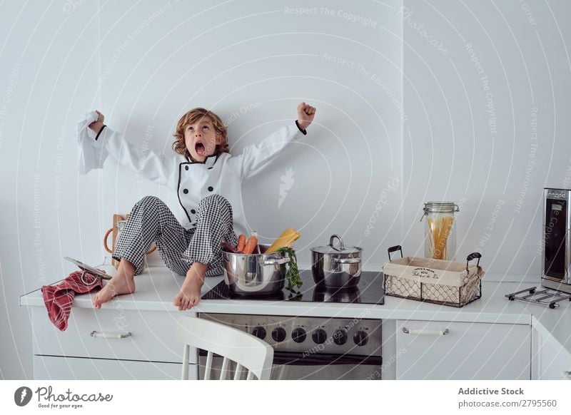 Junge mit Kochmütze neben Töpfen auf der Elektrofritteuse in der Küche sitzend Topf Küchenchef Kind Gemüse Hut Herd & Backofen kochen & garen modern lustig