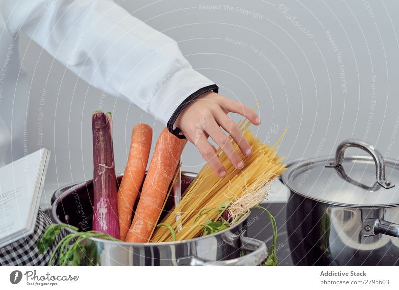 Junge in der Nähe des Topfes mit Gemüse und Nudeln auf der Elektrofritteuse in der Küche Koch Spätzle Küchenchef Kind Hand Herd & Backofen kochen & garen Putten