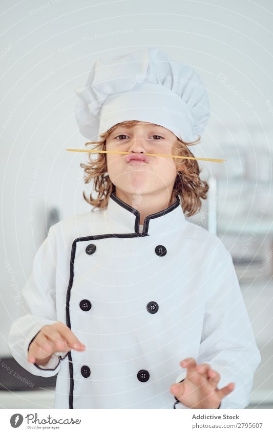 Junge mit Kochmütze, der in der Küche einen Schnurrbart aus Makkaroni macht. Oberlippenbart Küchenchef Kind Hut Spätzle regenarm machen kochen & garen modern