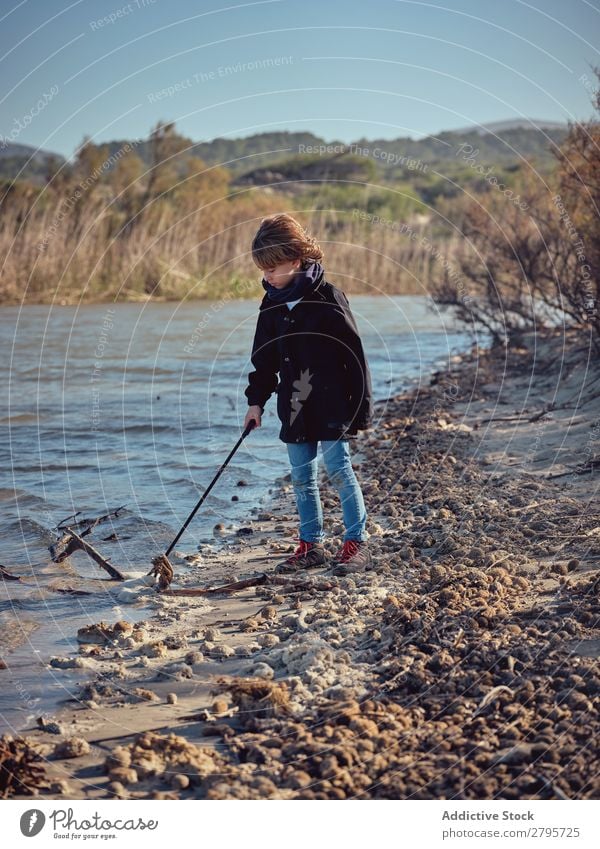 Junge mit Müllabfuhr, der Müll vom Flussufer aufhebt. Müllbehälter Abfall Kommissionierer abholend Küste Kind Wasser Aufräumen Umwelt Natur Freiwilliger