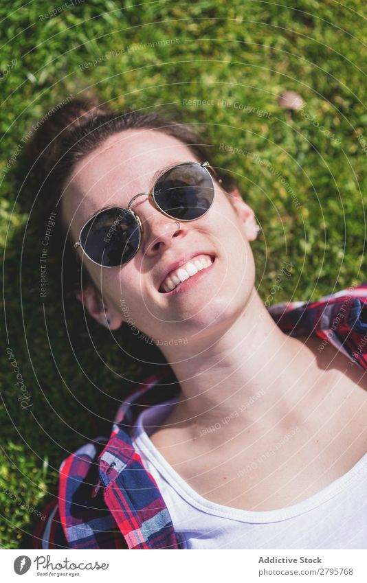 Oben die junge lächelnde Hipsterfrau, die an einem sonnigen Tag im Park auf Gras liegt und dabei mit dem Handy ein Selfie nimmt. obere Ansicht Junge Frau