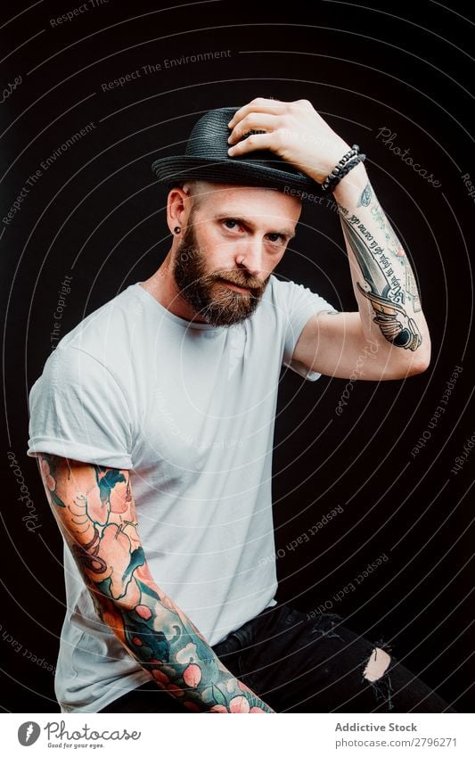 Lächelnder junger Mann mit Hut Schickimicki Tattoo Jugendliche Typ bärtig T-Shirt Hand heiter lässig Glück gutaussehend Coolness Stil trendy Studioaufnahme