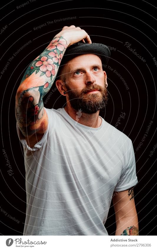 Lächelnder junger Mann mit Hut Schickimicki Tattoo Jugendliche Typ bärtig T-Shirt Hand heiter lässig Glück gutaussehend Coolness Stil trendy Studioaufnahme