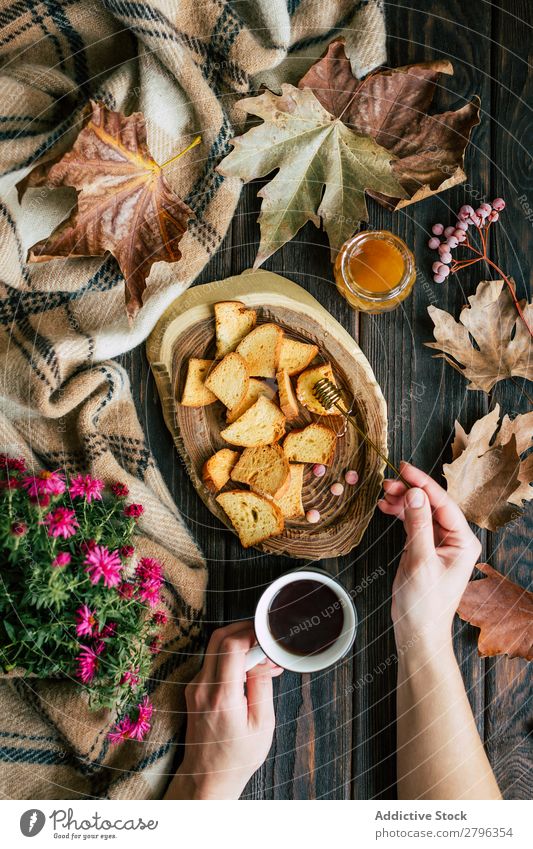 Hände mit teeverschmiertem Honig auf Croutons pflanzen. Hand Tee Schmiererei Blatt Herbst Blume Tisch Decke Löffel Tasse heiß trinken Getränk natürlich