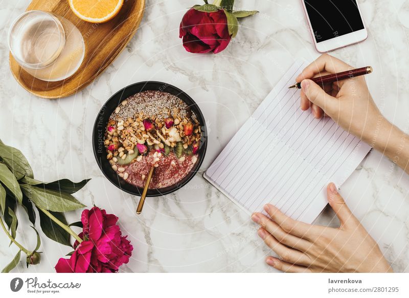 Flatlay von Frauenhänden mit Notebook und Smartphone, vegane Smoothie-Schüssel mit Chiapudding PDA organisch Zutaten Schreibstift Aussicht Top Murmel Snack