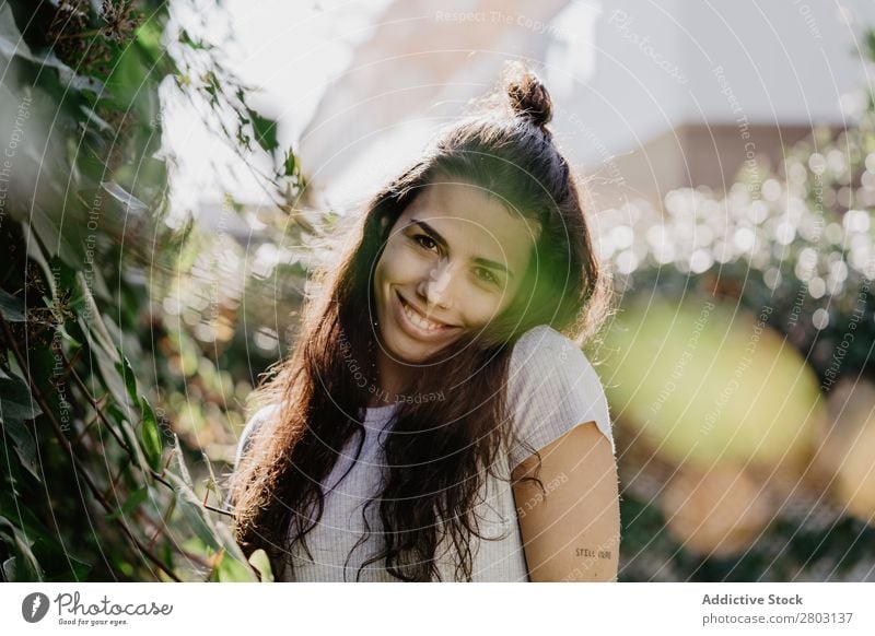 Fröhliche Frau im Garten Hinterhof brünett Lächeln Sträucher Jugendliche Sonnenstrahlen Tag gestikulieren Sommer Stil lässig trendy Park harmonisch Idylle Glück