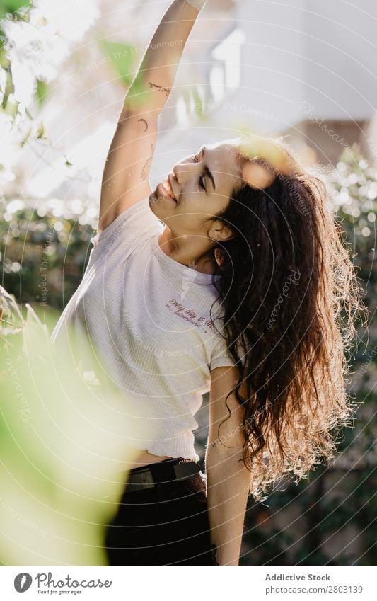 Fröhliche Frau im Garten Hinterhof brünett Lächeln Sträucher Jugendliche Sonnenstrahlen Tag gestikulieren Sommer Stil lässig trendy Park harmonisch Idylle Glück