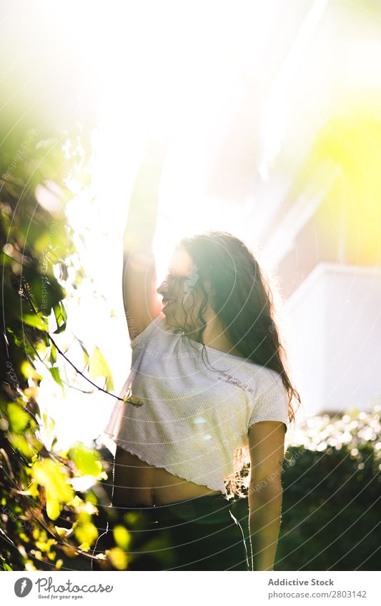 Fröhliche Frau im Garten Hinterhof brünett Lächeln Sträucher Jugendliche Sonnenstrahlen Tag gestikulieren Sommer Stil lässig trendy Park harmonisch Idylle Glück