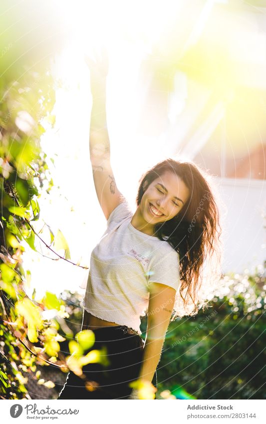 Fröhliche Frau im Garten Hinterhof brünett Lächeln Sträucher Jugendliche Sonnenstrahlen Tag gestikulieren Sommer Stil lässig trendy Park harmonisch Idylle Glück