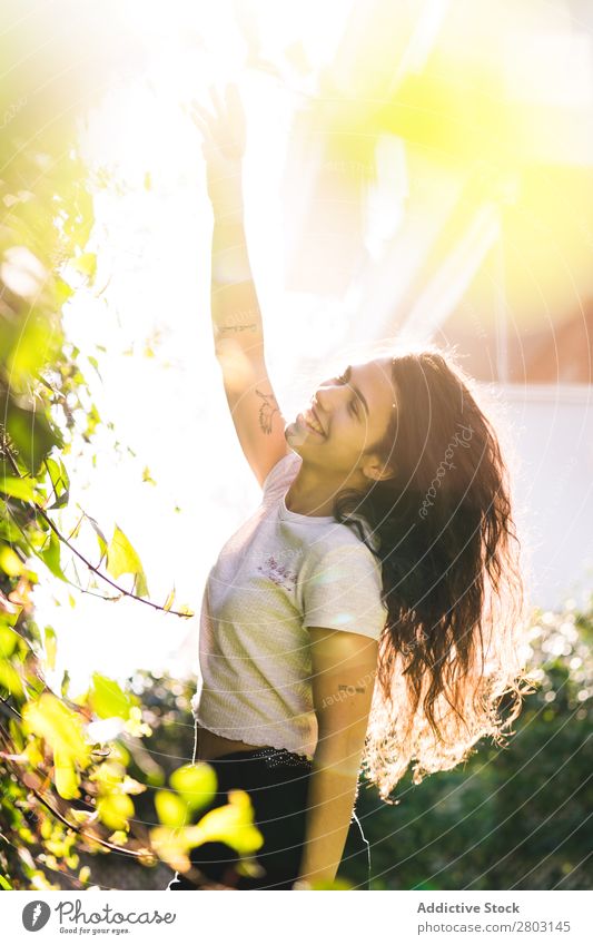 Fröhliche Frau im Garten Hinterhof brünett Lächeln Sträucher Jugendliche Sonnenstrahlen Tag gestikulieren Sommer Stil lässig trendy Park harmonisch Idylle Glück