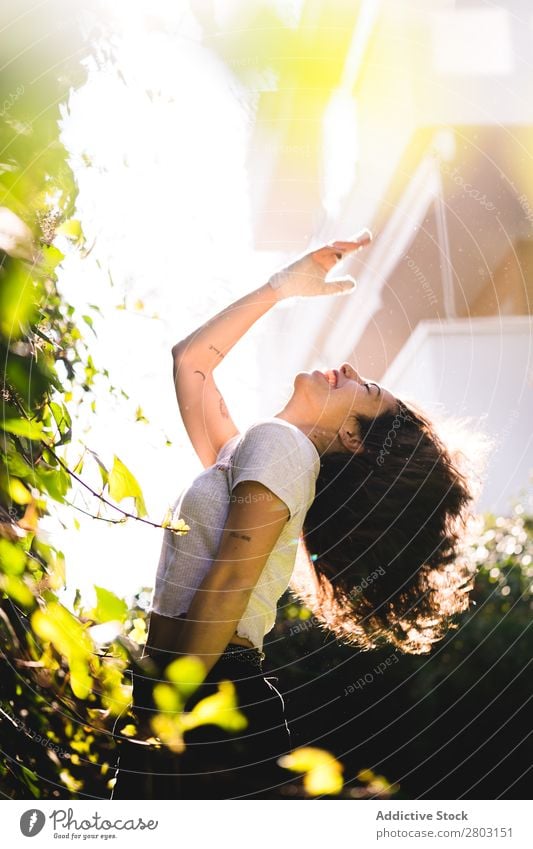 Fröhliche Frau im Garten Hinterhof brünett Lächeln Sträucher Jugendliche Sonnenstrahlen Tag gestikulieren Sommer Stil lässig trendy Park harmonisch Idylle Glück