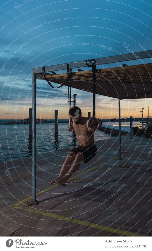 Athletischer Mann balanciert auf Gymnastikringen Sportler Gleichgewicht gymnastisch Stauanlage Ring ohne Hemd Wasser Großstadt Abend sportlich Jugendliche