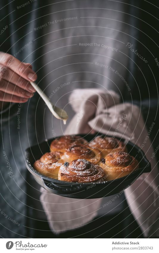 Getreidefrau, die Sauce zu Zimtrollen hinzufügt. Frau Saucen Zimtbrötchen Brötchen Löffel hinzufügen Pfanne Lebensmittel Mahlzeit frisch rustikal Feinschmecker