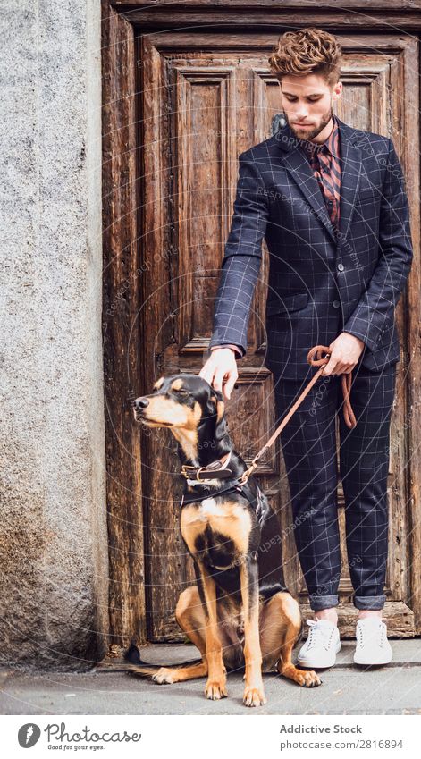 Schöner eleganter junger Modemann im trendigen Kostümanzug mit Hund, alter Holztürhintergrund Anzug Mann Herr modisch Bekleidung Stil Model Hemd Hand lässig