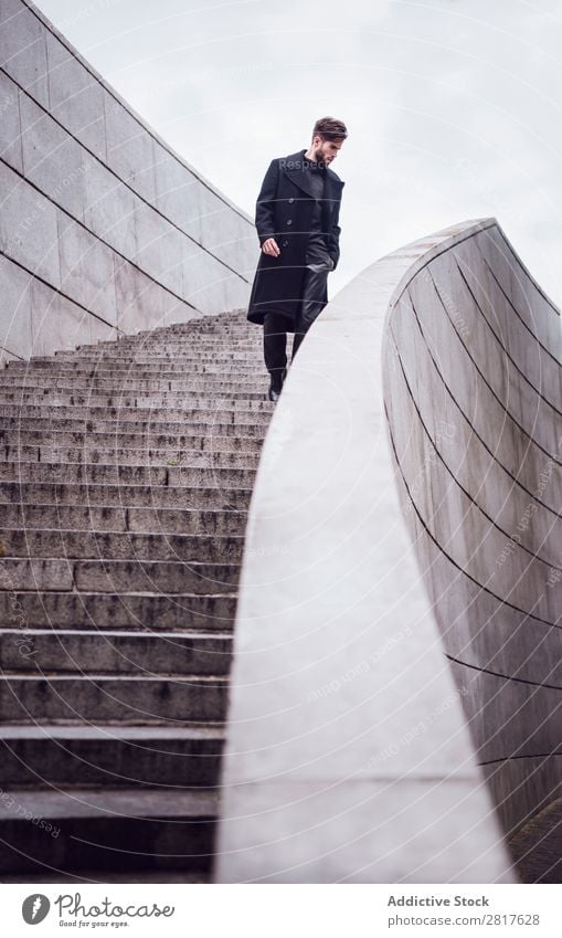 Junger, gutaussehender, trendiger Mann mit Mantel, der auf der Treppe posiert. Erwachsene attraktiv Vollbart bärtig lässig Kaukasier Coolness niedlich tief