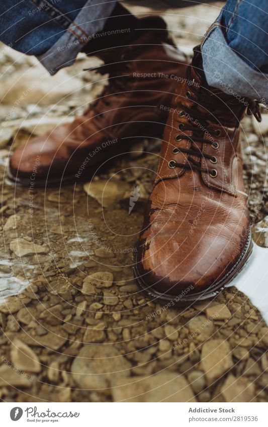 Beine in Lederstiefeln in der Pfütze Stiefel Natur Wanderer braun Stil wandern Abenteuer Stein Kieselsteine Trekking Aktion Jeansstoff Jeanshose Fuß laufen