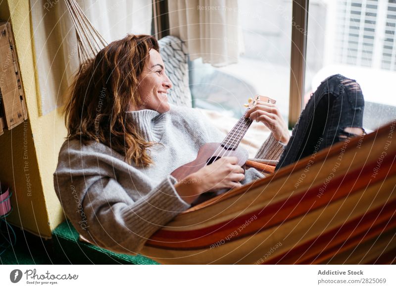 Fröhliche Frau beim Ukulelele spielen heimwärts Erholung Spielen Lifestyle Musiker heiter Lächeln schön Raum Mensch lässig Erwachsene Haus Beautyfotografie