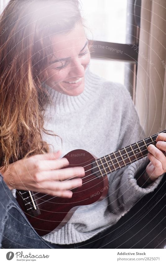 Fröhliche Frau beim Ukulelele spielen heimwärts Erholung Spielen Lifestyle Musiker heiter Lächeln schön Raum Mensch lässig Erwachsene Haus Beautyfotografie