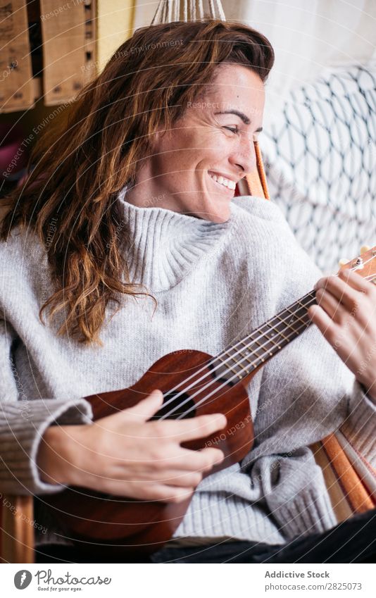 Fröhliche Frau beim Ukulelele spielen heimwärts Erholung Spielen Lifestyle Musiker heiter Lächeln schön Raum Mensch lässig Erwachsene Haus Beautyfotografie